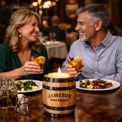 Custom logo oak barrel candle holder on restaurant table with couple enjoying cocktails, distillery promotional product enhancing brand experience