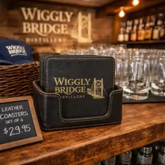 Custom leather coaster set in holder displayed in a distillery gift shop with barware and merchandise, perfect for retail and promotional products