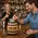 Custom logo oak barrel tip jar on a busy bar with bartenders making drinks and whiskey bottles in the background, designed for bar branding and promotions