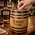 Engraved Larceny Fund oak barrel piggy bank with coin slot on a distillery bar as a hand drops a coin in, showcasing branded distillery gift shop merchandise