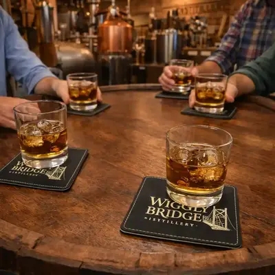 Personalized leather coasters used in a distillery tasting room with whiskey glasses, highlighting custom bar accessories and branded merchandise