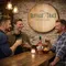 Custom Buffalo Trace style barrel head sign mounted in a rustic home bar with men enjoying whiskey and branded bottle on bar