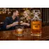 Crystal whiskey decanter and single rocks glass on a home bar with a couple enjoying drinks in the background